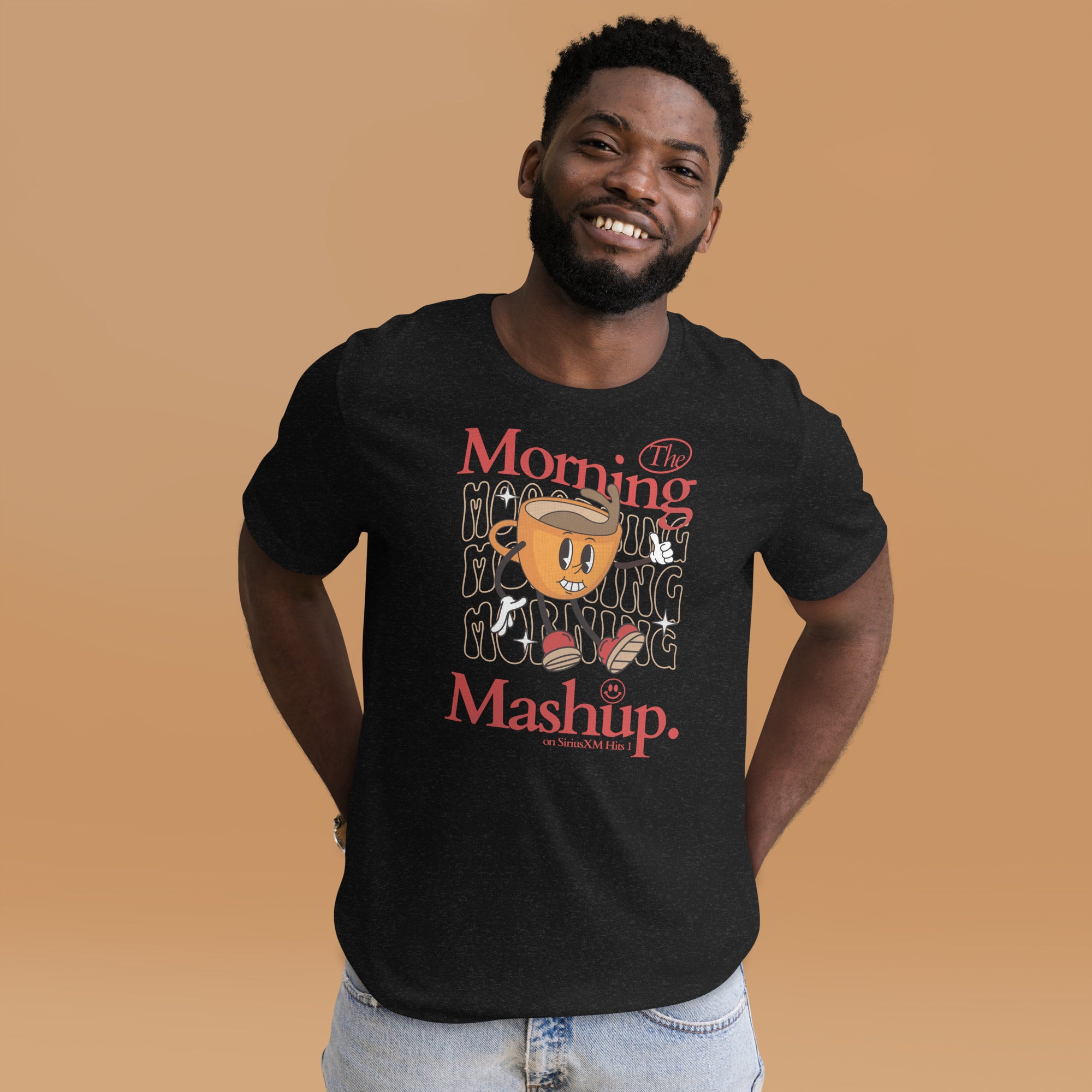 Man smiling while wearing a graphic T-shirt featuring a retro-style cartoon coffee cup character with arms, legs, and red sneakers, standing in front of wavy 'Morning' text. Bold red and white lettering reads 'The Morning Mashup on SiriusXM Hits 1.'