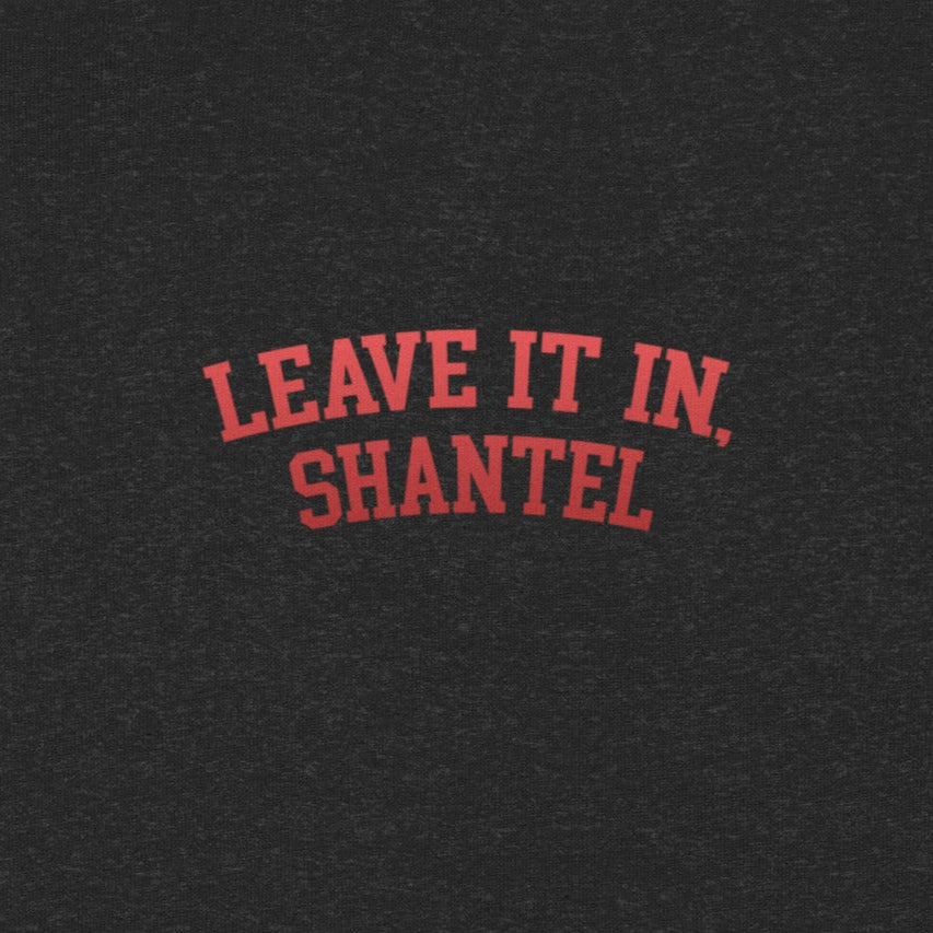 A close-up view of a black heather fabric showing red arched text printed on it. The text reads 'LEAVE IT IN, SHANTEL' in bold, all-caps lettering.
