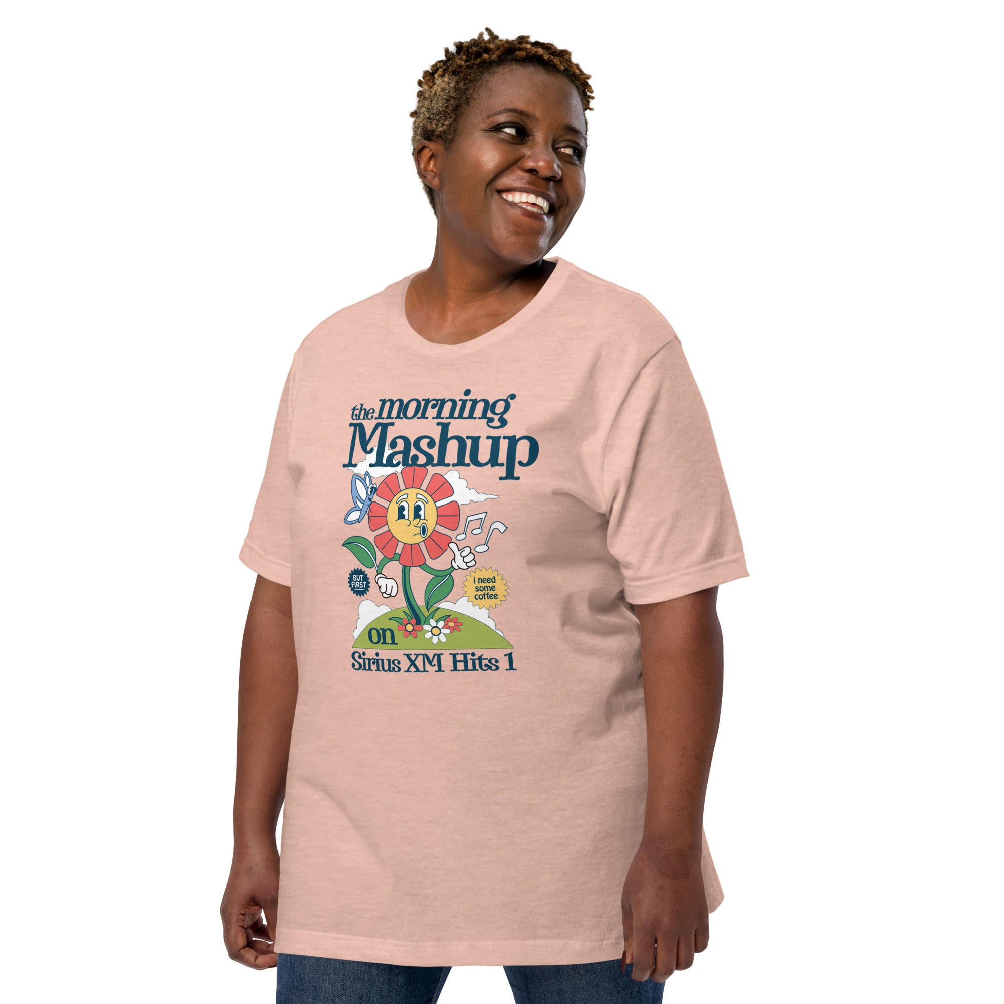 Woman smiling while wearing a peach-colored T-shirt with a large cartoon graphic of a flower character and the words 'the morning Mashup on Sirius XM Hits 1.'