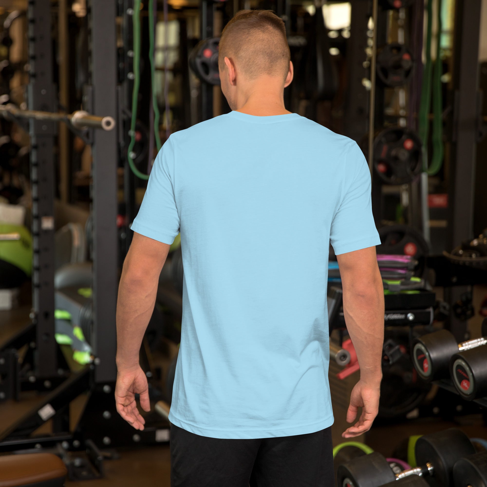 Man standing in a gym with his back to the camera, wearing a plain light blue T-shirt with no visible graphics or text.