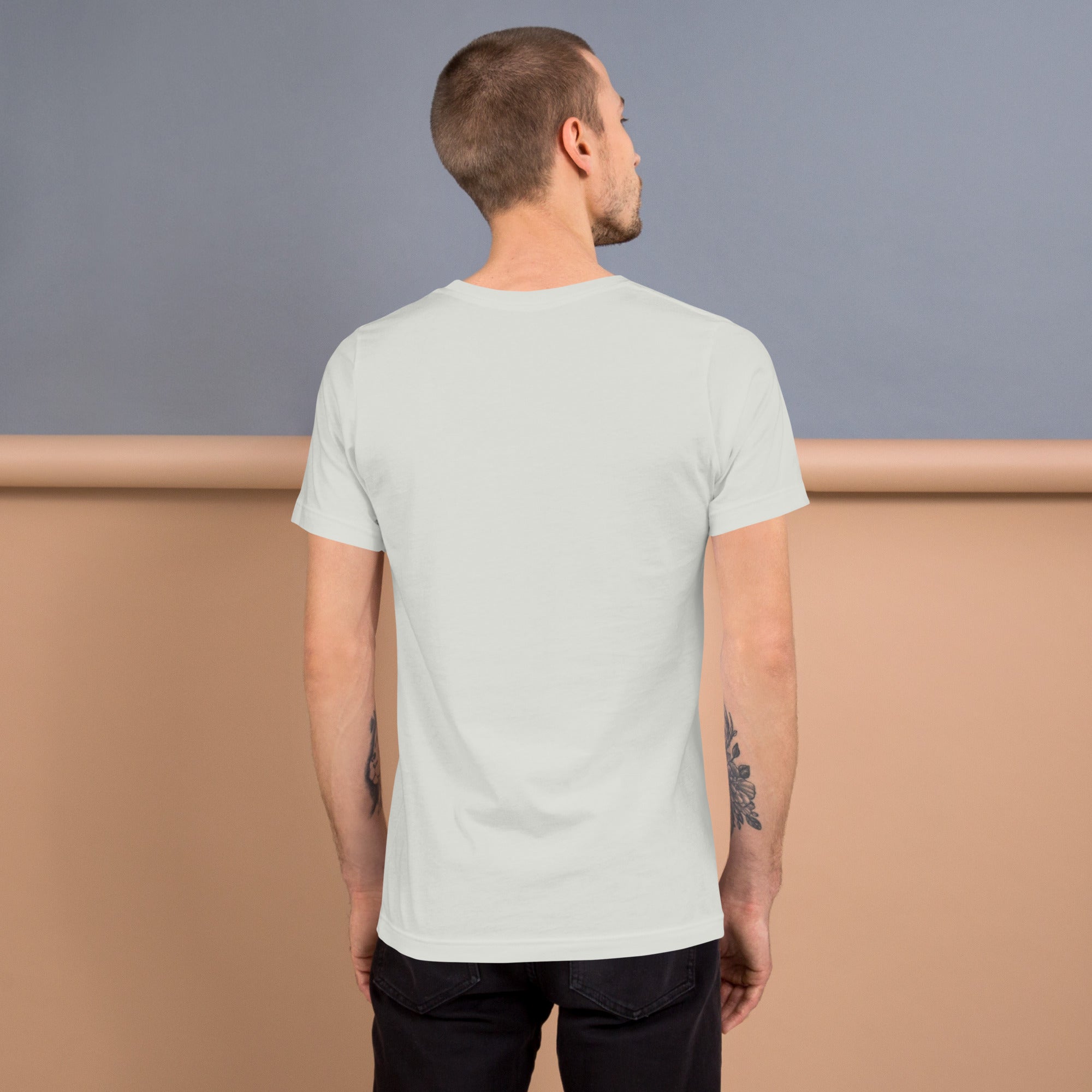 Man standing with his back to the camera, wearing a plain silver T-shirt with no design, in front of a tan and gray background.