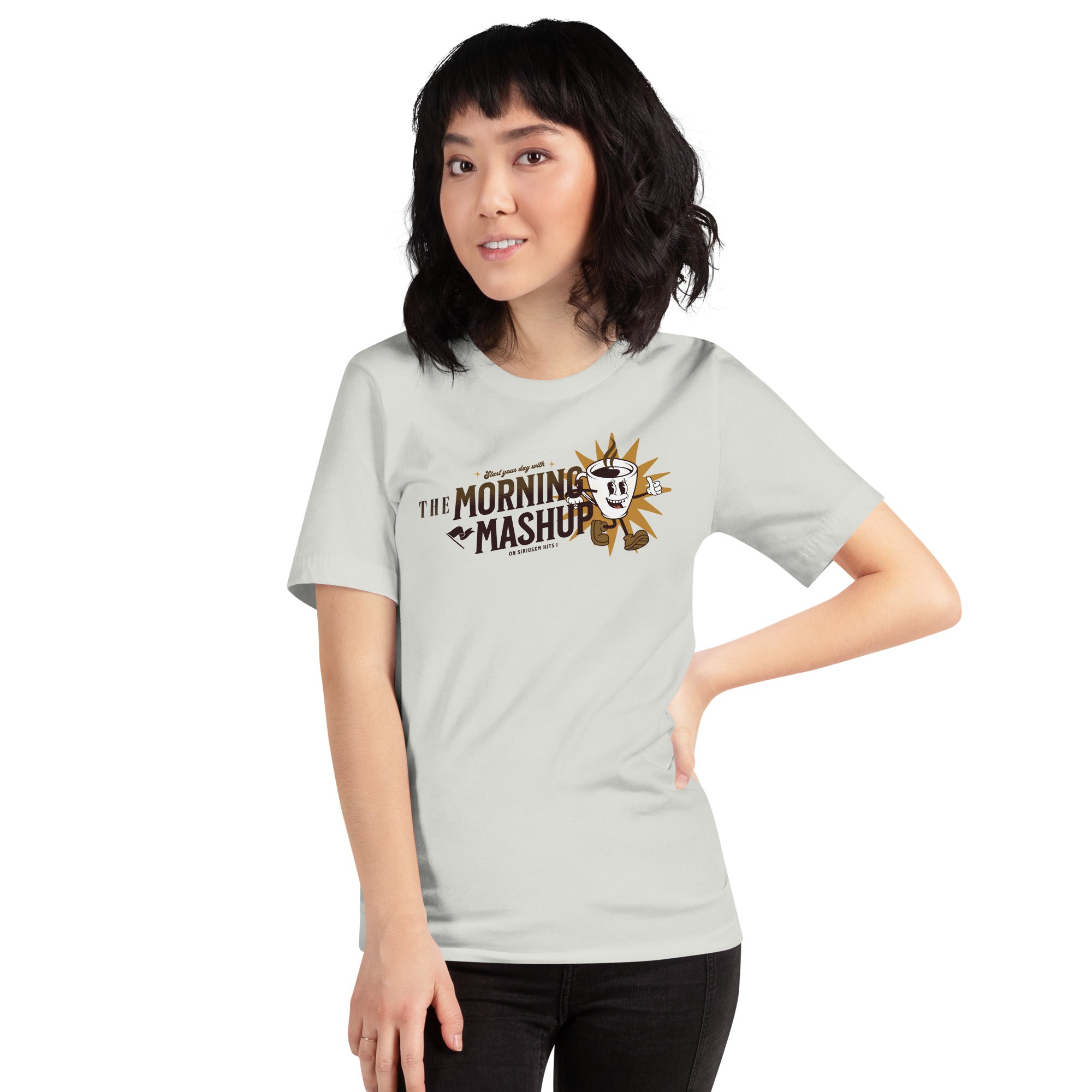 Woman smiling and wearing a light silver T-shirt with a vintage-style graphic of a coffee mug character in front of a golden sunburst, and the words 'THE MORNING MASHUP on SiriusXM Hits 1.'