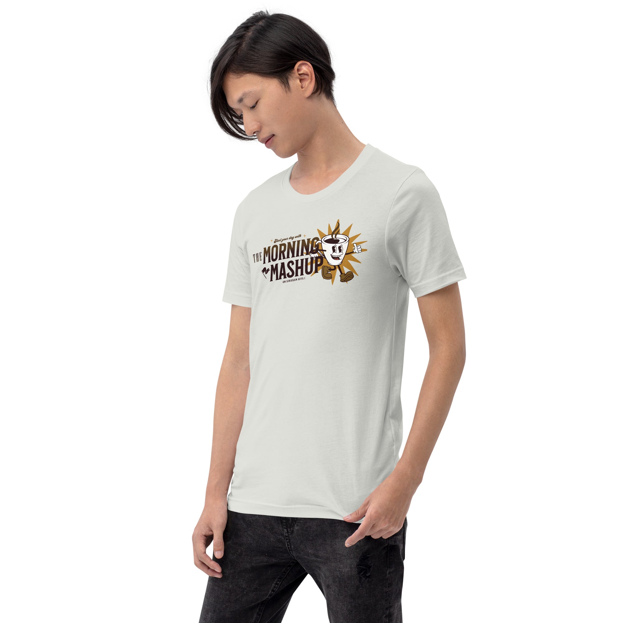 Man looking down while wearing a light silver T-shirt with a retro coffee mug mascot giving a thumbs-up, positioned beside bold text that reads 'THE MORNING MASHUP on SiriusXM Hits 1' in brown and gold.