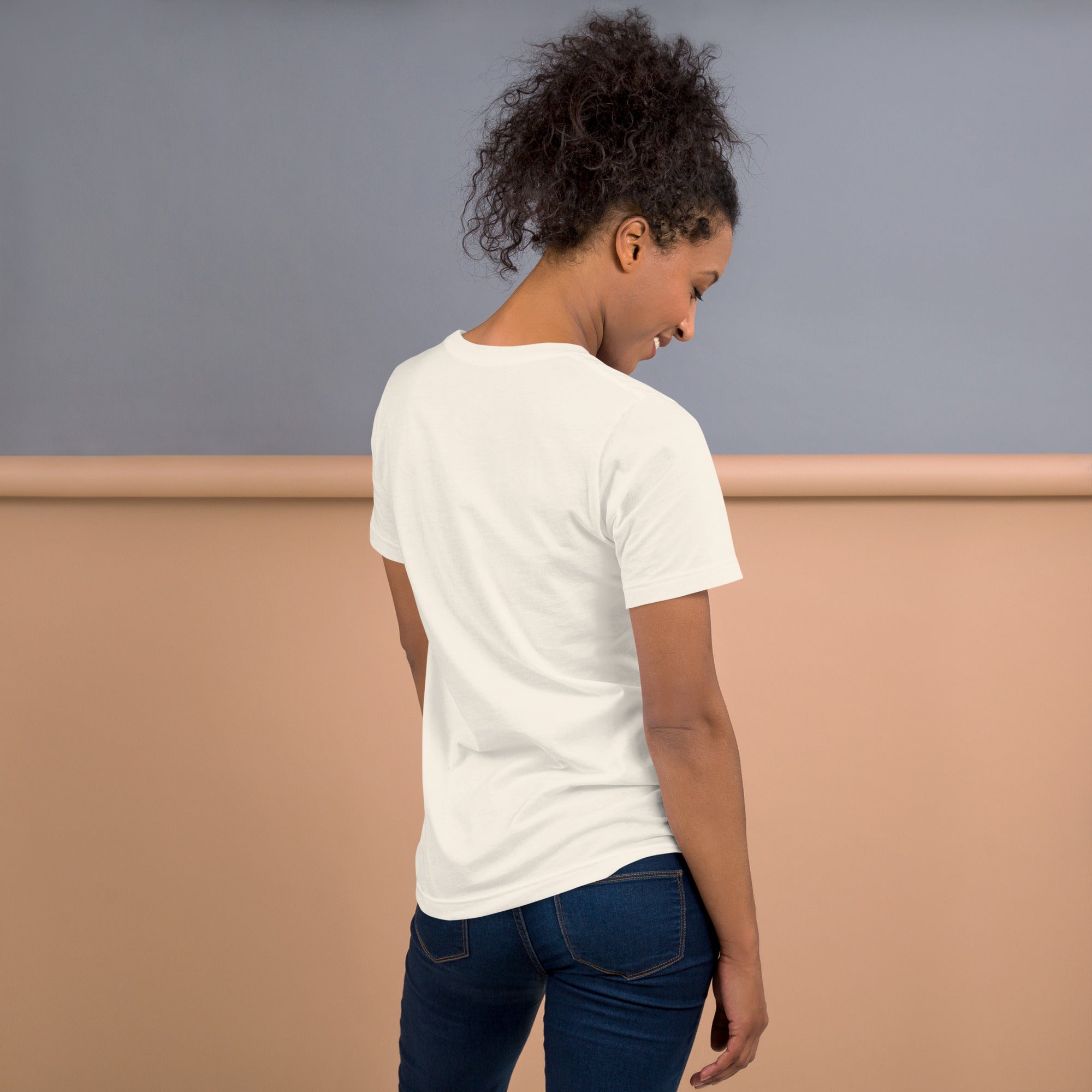 A woman wearing a short-sleeve vintage white T-shirt viewed from the back, standing in front of a peach and gray backdrop.