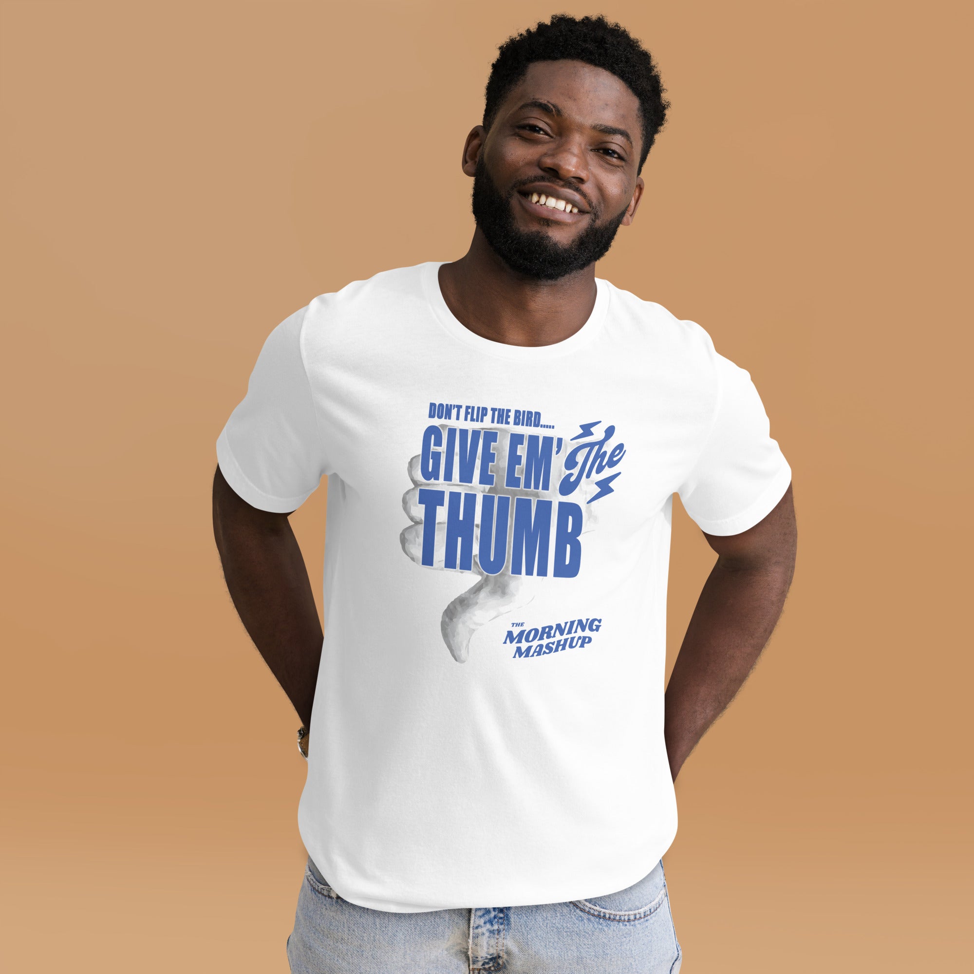 Man smiling while wearing a white T-shirt with blue graphic text that reads 'DON’T FLIP THE BIRD... GIVE EM’ THE THUMB' and 'THE MORNING MASHUP,' featuring a large thumbs-down illustration.