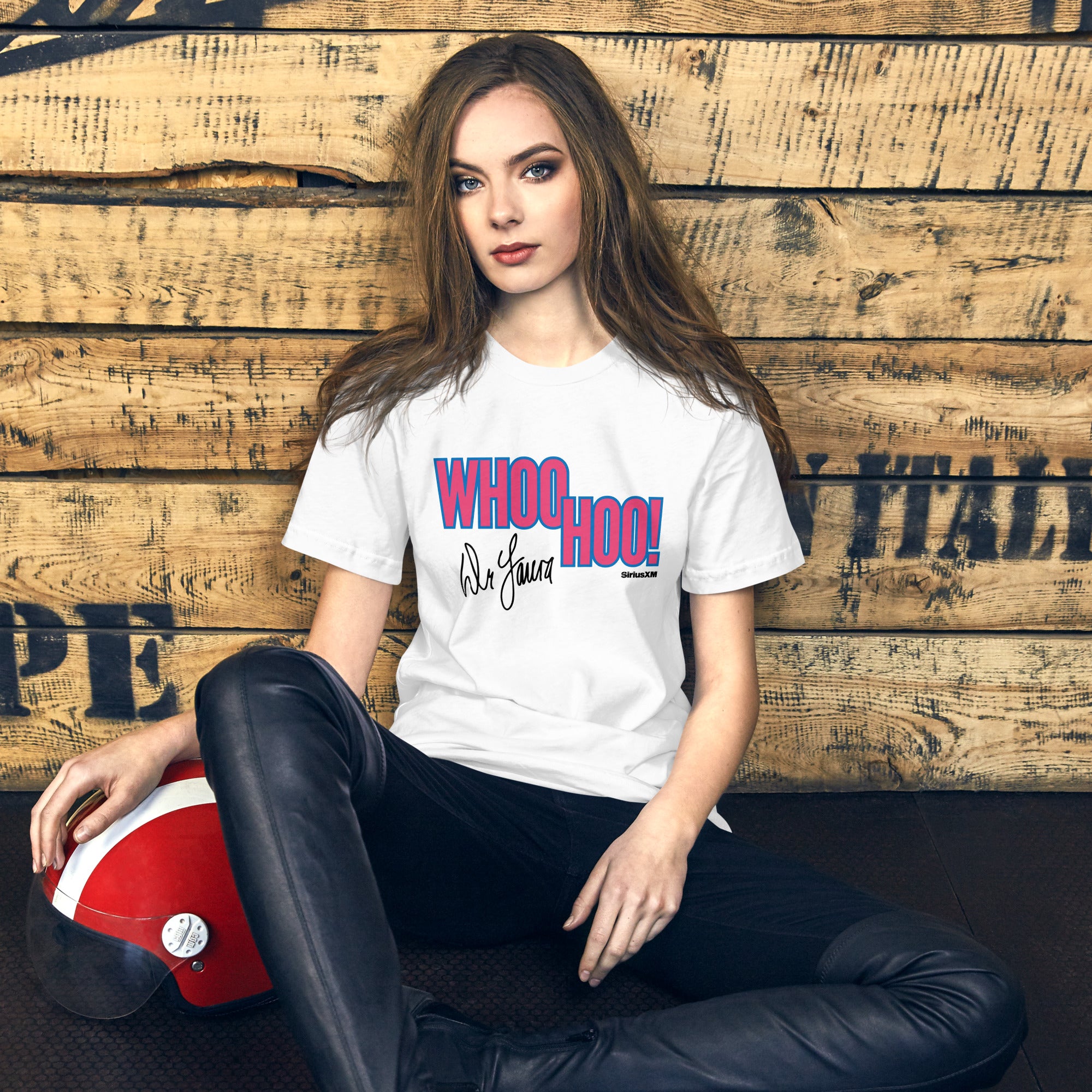 A woman with long hair sits on the floor leaning against a wooden wall while wearing a white t-shirt that says 'WHOO HOO!' in pink and blue letters, with 'Dr. Laura' in script and the 'SiriusXM' logo beneath the graphic.