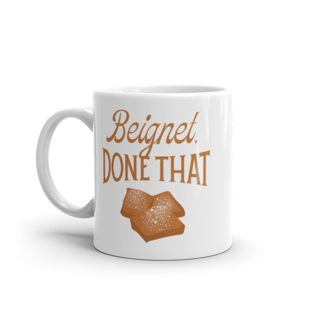 White coffee mug featuring the text 'Beignet. DONE THAT' with images of powdered beignets with the handle on the left.
